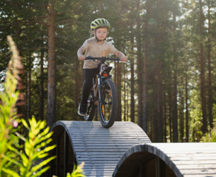 Barn cyklar över vågformad skills trail i skog