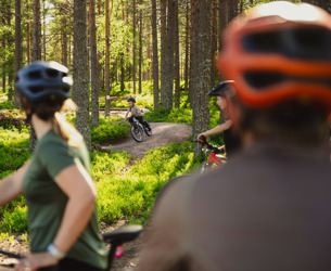 A family is cycling through a forest, with focus on a child riding ahead of the adults.