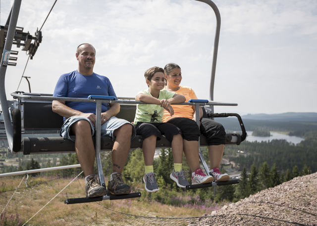 Familj sitter i stolslift över skog och sjölandskap