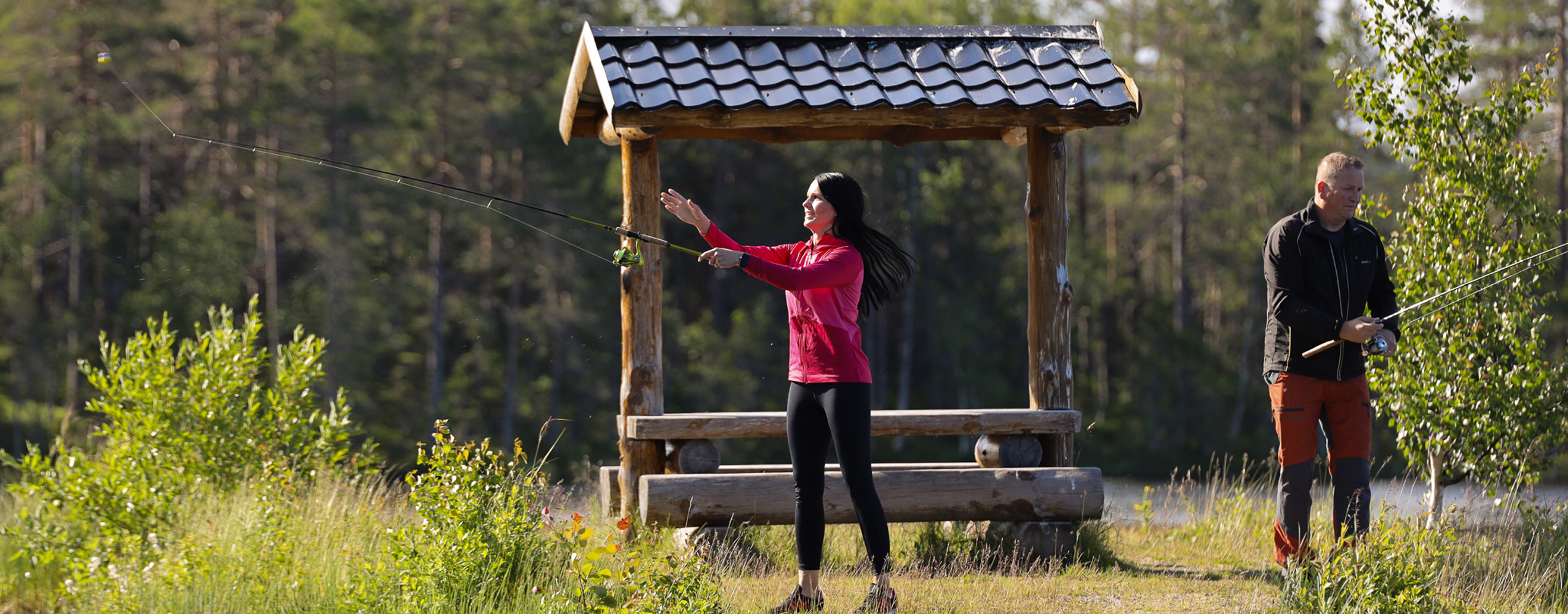 En kvinna kastar ut fiskespö vid en stilla sjö medan en man står bredvid.