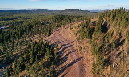 Flygbild över ett skogsklätt bergsområde med en bred grusväg som slingrar sig längs sluttningen i Orsa Grönklitt.