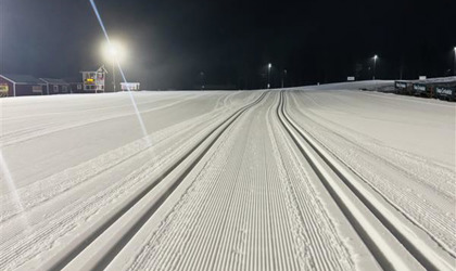 Nypreparerade längdskidspår på en upplyst stadion i mörker, med lampor och byggnader i bakgrunden.