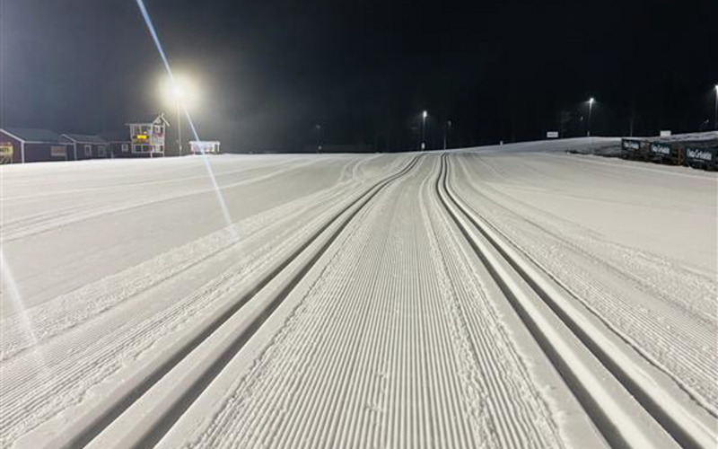 Nypreparerade längdskidspår på en upplyst stadion i mörker, med lampor och byggnader i bakgrunden.