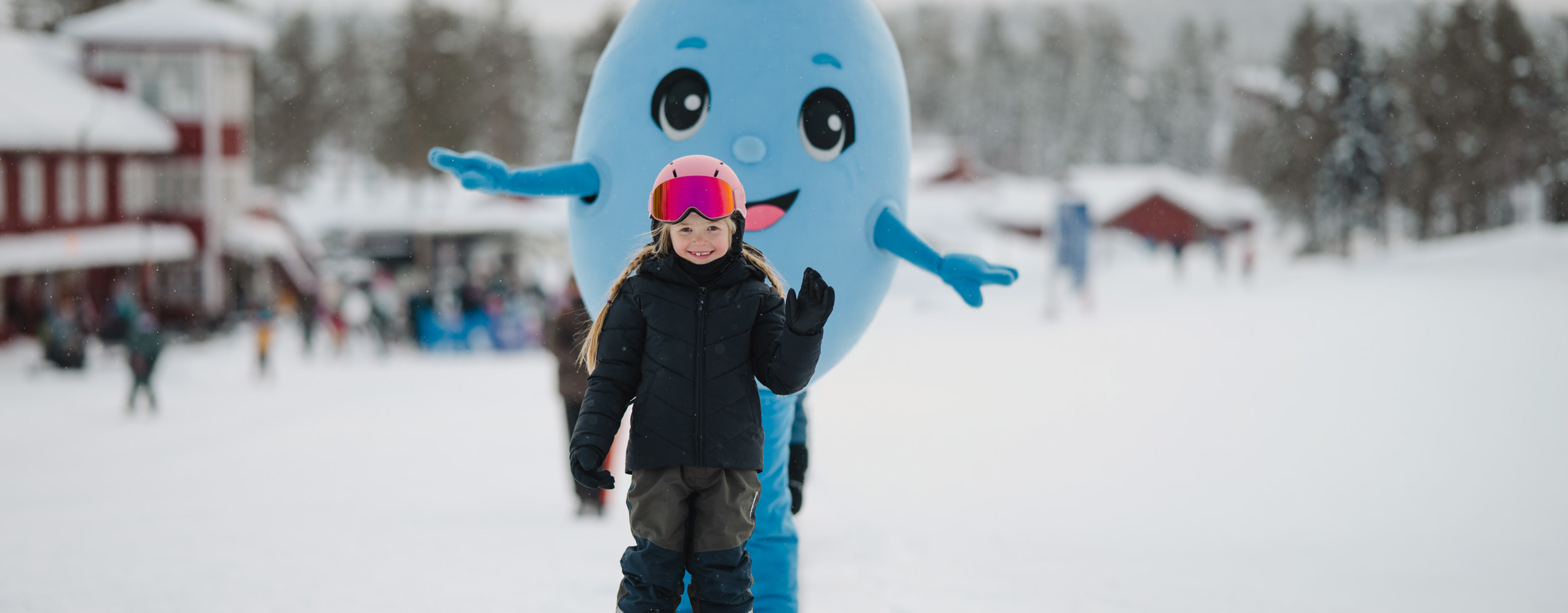 Barn på alpina skidor tillsammans med Bärra Blåbär i ett snötäckt vinterlandskap.