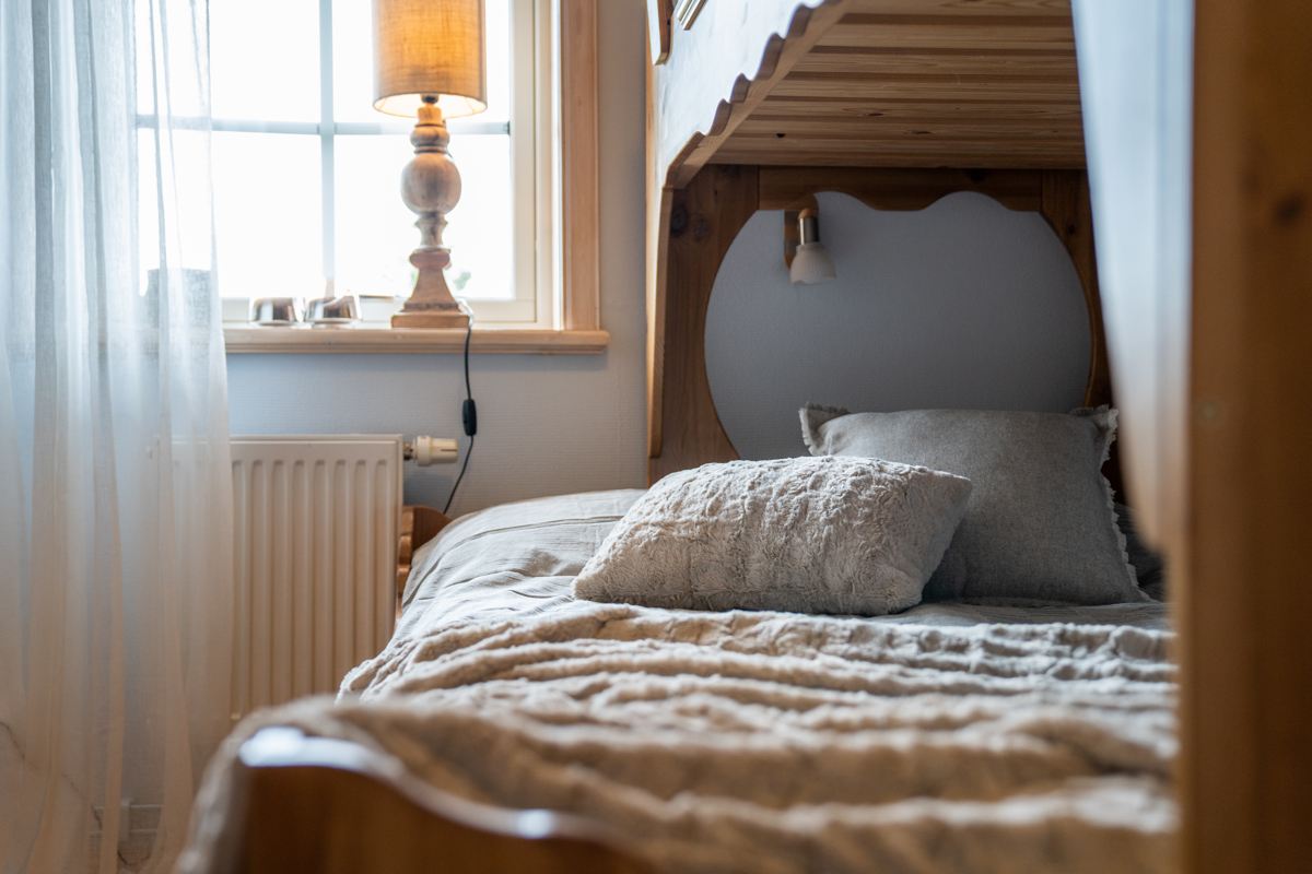 Bäddad underslaf i våningssäng med kudde och filt bredvid ett fönster med lampa.