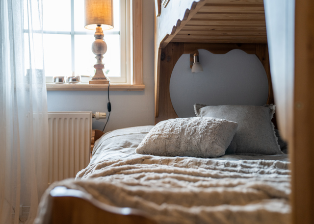 Made lower bunk bed with pillow and blanket next to a window with a lamp.