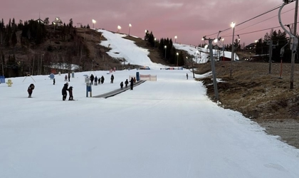 Alpin skidbacke med åkare i nedfarten och liftar längs sidan i skymningsljus.