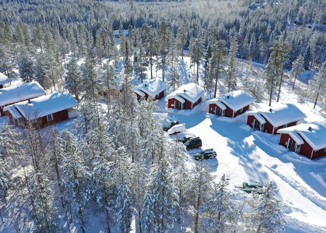 Flygfoto över röda stugor med snötäckta tak i skogsmiljö, vintertid.