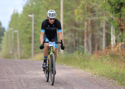En ung cyklist med tävlingsnummer cyklar på en grusväg omgiven av träd.