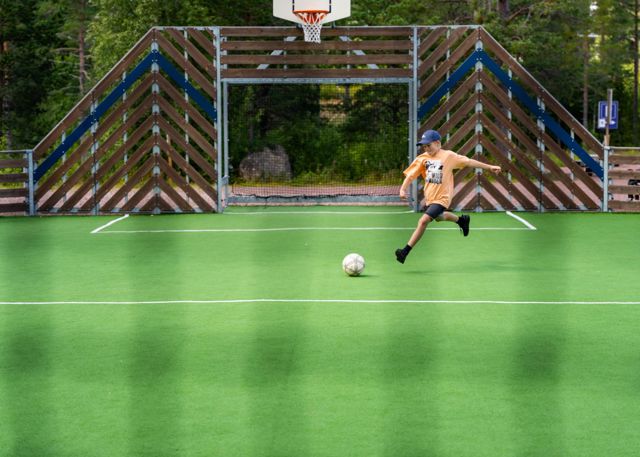 Barn spelar fotboll på en konstgräsplan med mål och basketkorg.