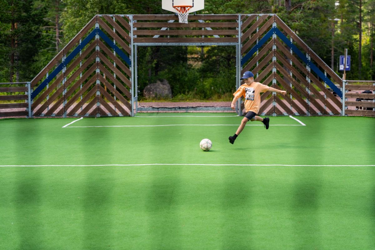 Child playing soccer on an artificial turf field with goal and basketball hoop.