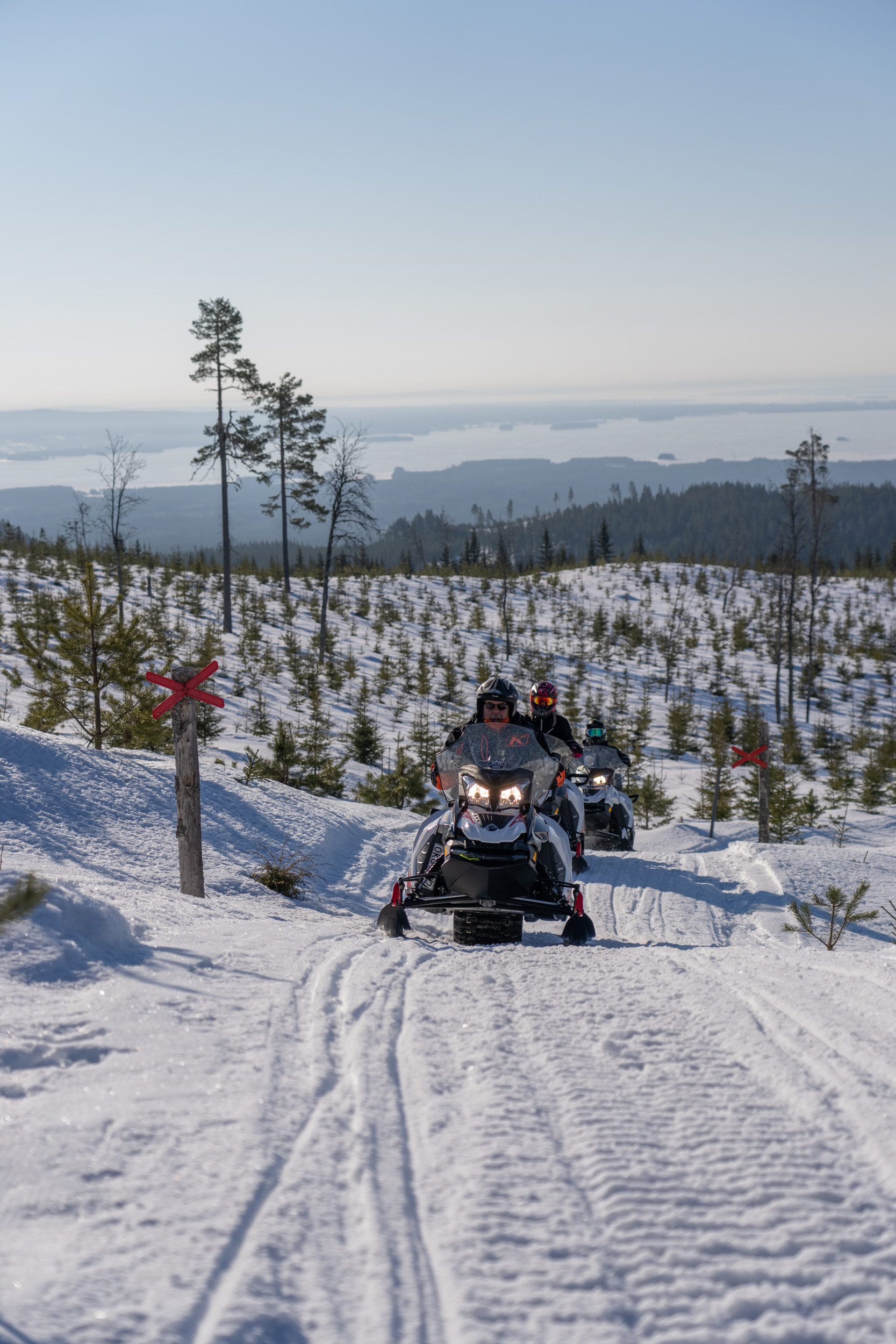 Tre personer sitter på snöskotrar i snön och njuter av solen över ett öppet vinterlandskap.