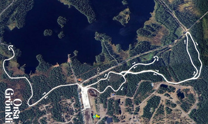 Flygbild i kartvy som visar vägar och markerade leder i ett skogsområde intill en sjö.