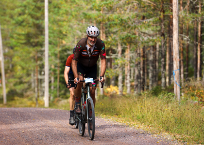 En äldre manlig cyklist med skägg och hjälm cyklar på en grusväg i skogen.