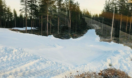 Smalt preparerat snöspår som löper genom barrskog med barmark vid sidan.