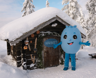 Blå figur står utanför en snötäckt timmerstuga med skylt på dörren i vintermiljö.