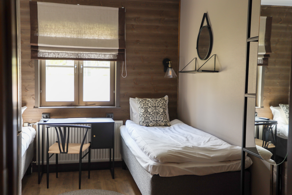 Litet sovrum med enkelsäng, skrivbord och fönster med mörka ramar.