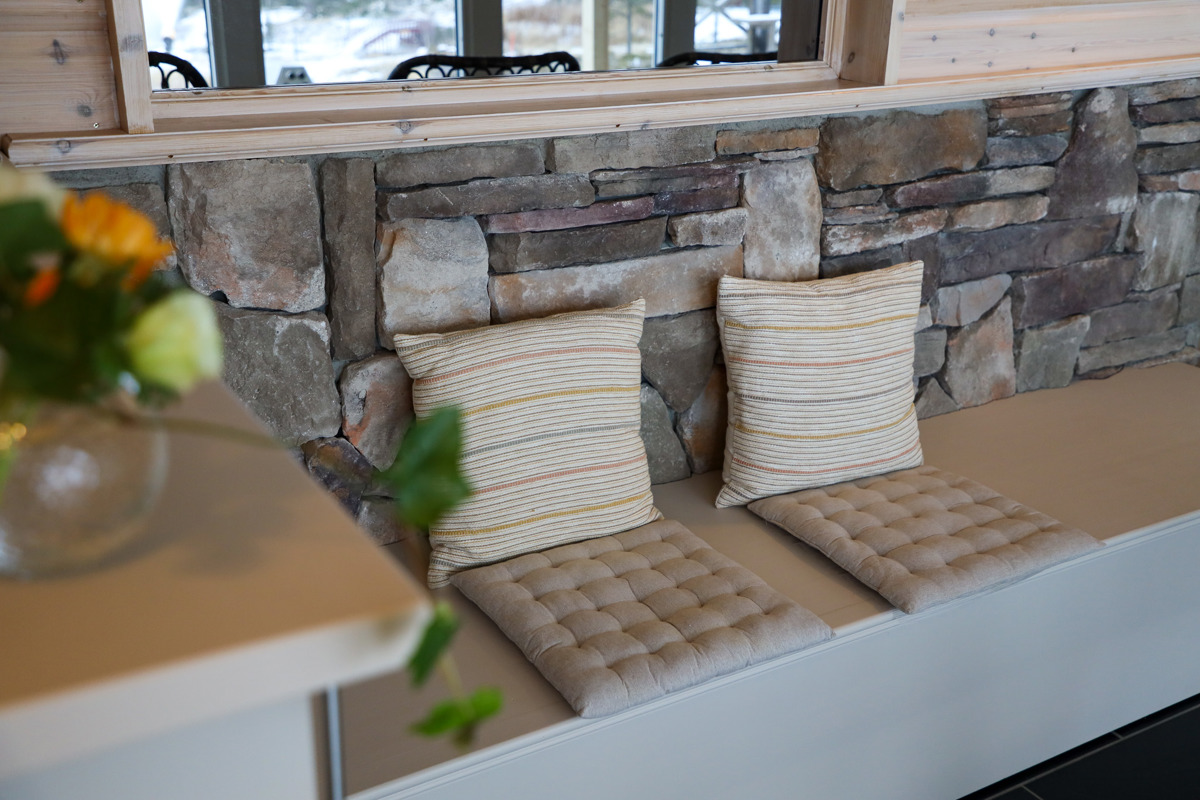 Bench with cushions and striped pillows against a natural stone wall.