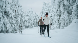 Två personer åker längdskidor på ett preparerat spår genom en snötäckt skog.