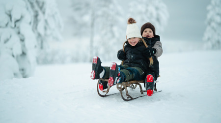 Two children sledding together in a snowy landscape with trees in the background.