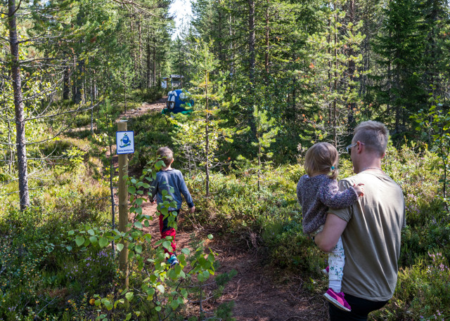 Children and adults walk after Bärra along a forest path.