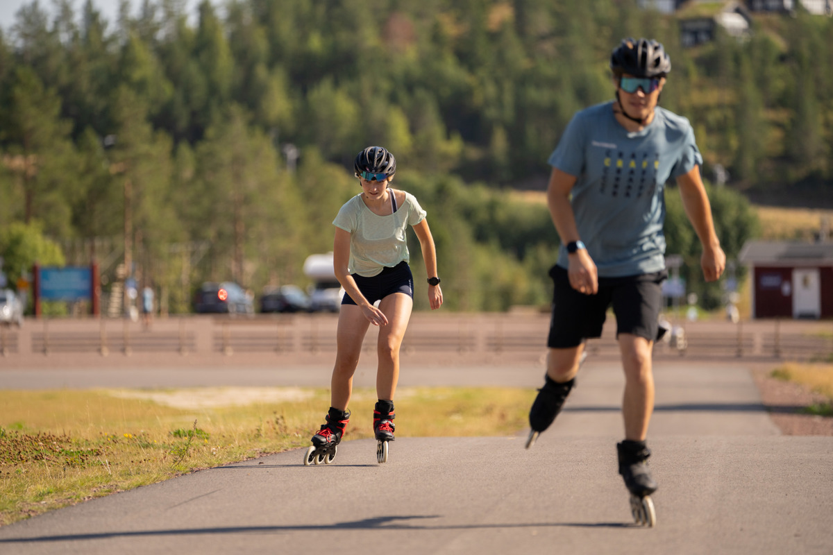 Two people rollerblading on a paved road in the summer sun.