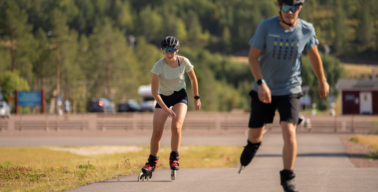 Two people rollerblading on a paved road in the summer sun.