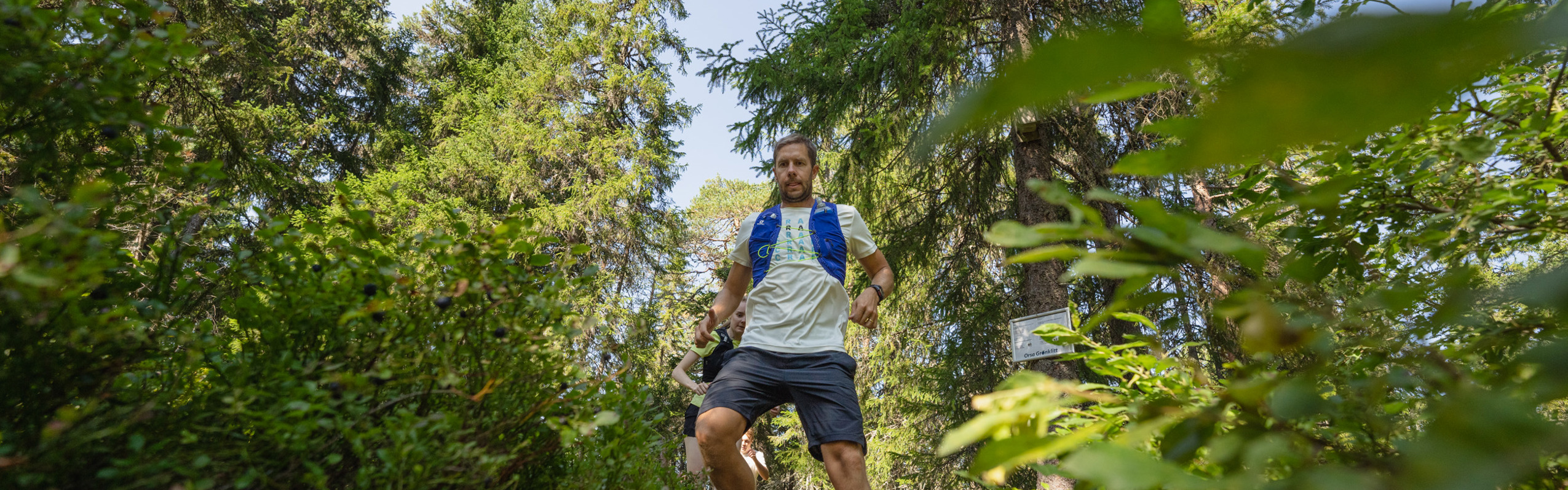 En man springer nedför en smal skogsstig omgiven av grönska