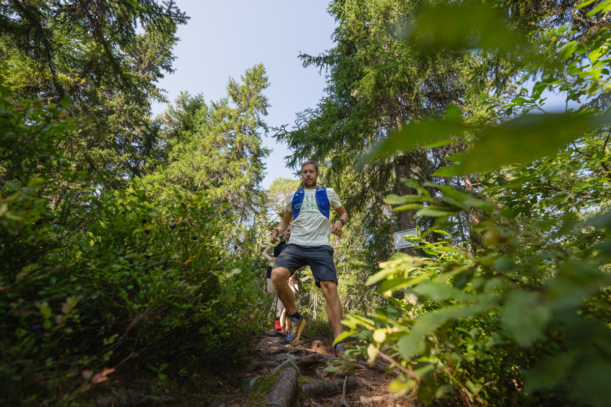 A man runs down a narrow forest trail surrounded by lush greenery.