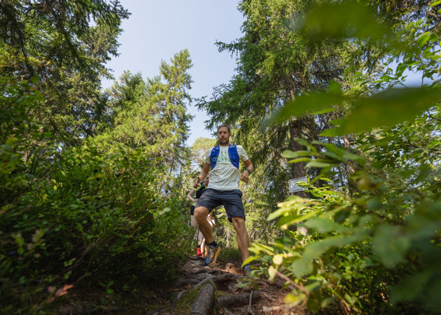 A man runs down a narrow forest trail surrounded by lush greenery.