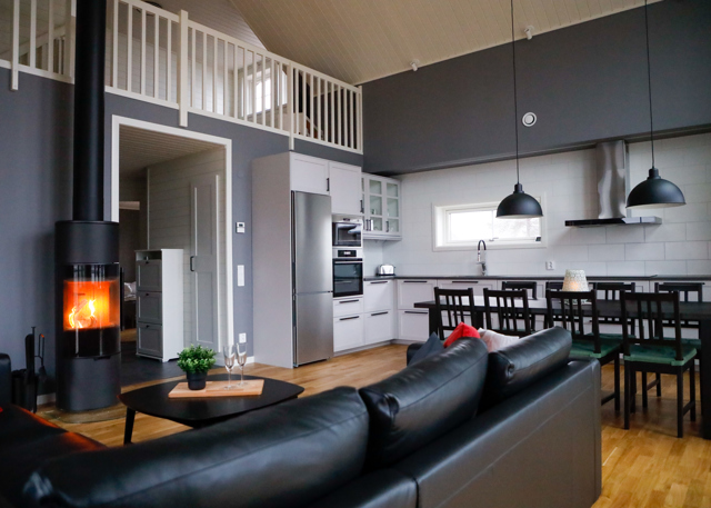 Modern living room and kitchen with black sofa, dining area, and wood-burning stove.