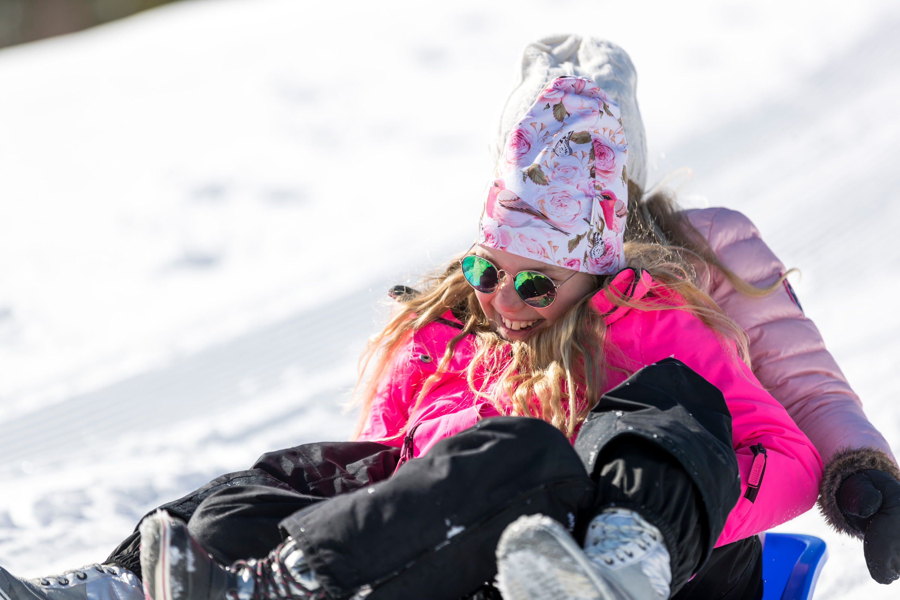 To børn i farverigt vintertøj kælker i solskin og griner sammen på en sneklædt bakke