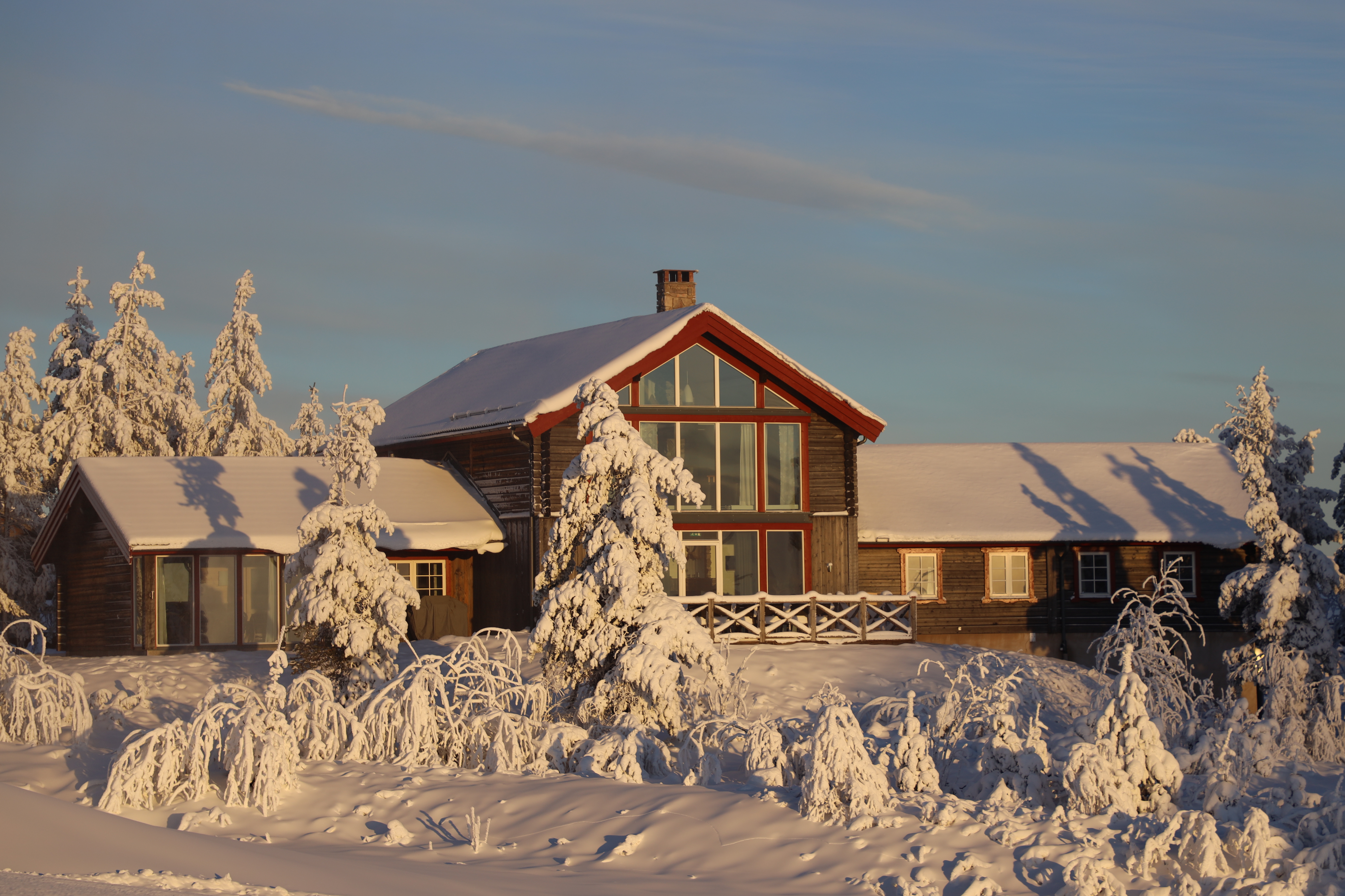 Large log cabin with big windows in a snow-covered mountain setting.