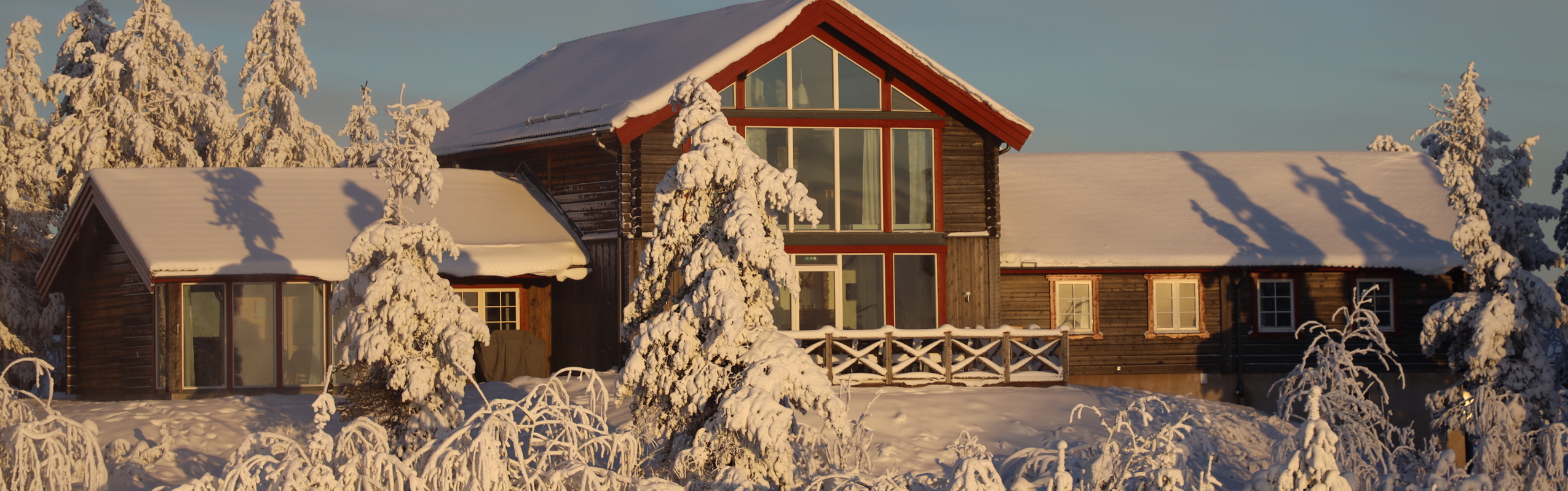 Large log cabin with big windows in a snow-covered mountain setting.