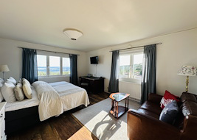 Bright bedroom with double bed, sitting area, and view through large windows.