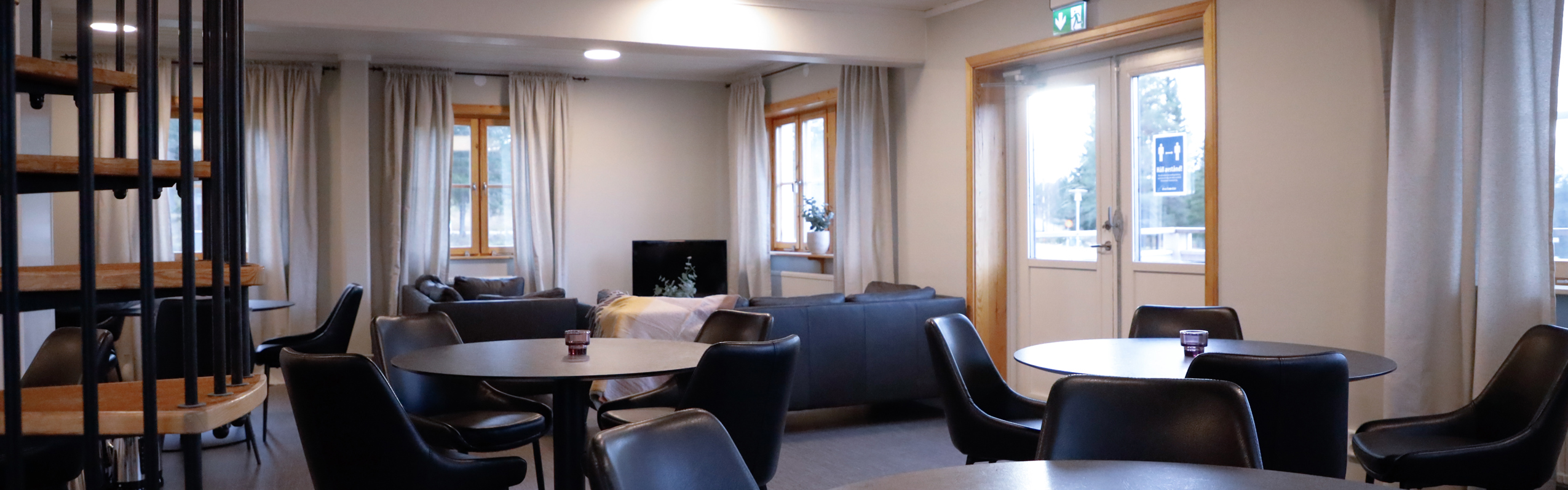 Common room with round tables, black chairs, spiral staircase, sofas, and a TV.