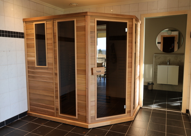 Wooden infrared sauna placed in a tiled room with black floor.