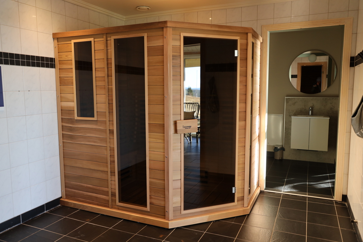 Infraröd bastu i trä placerad i helkaklat rum med svart golv.