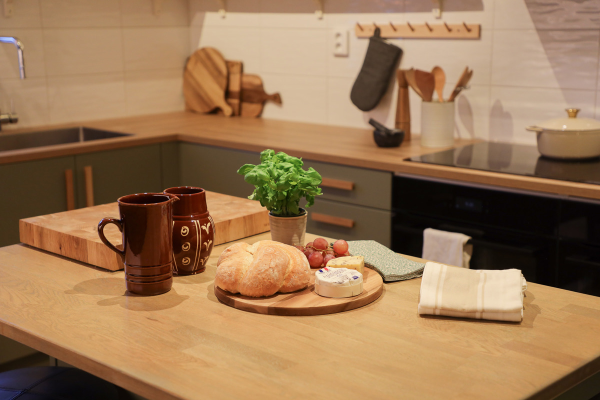 Kitchen counter with bread, cheese, herbs, and mugs in a cozy kitchen with wooden details.