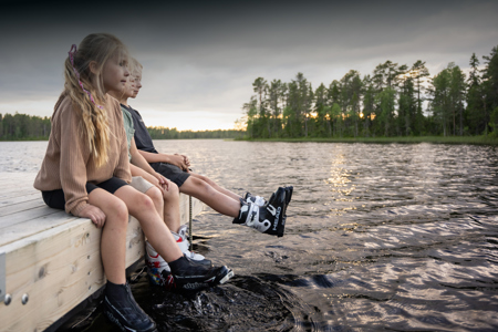 Barn sitter på en brygga med fötterna i vattnet vid en sjö.
