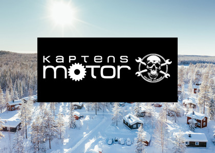 Logotyp för Kaptens Motor centrerad över en solig vinterbild med snötäckta stugor och skog i bakgrunden.