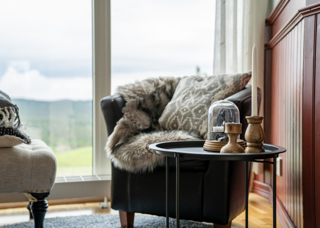 Armchair with cushion and throw next to a table with candlesticks by a large window.