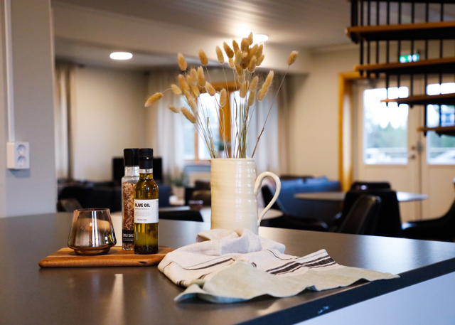 Køkkenø med kande med tørrede planter, krydderier og viskestykke i fællesrum.