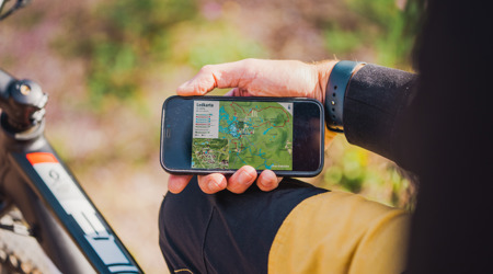 En person håller i en mobiltelefon med en öppen karta över leder, sittandes vid en cykel.