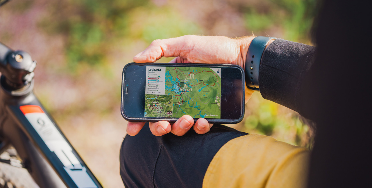 En person håller i en mobiltelefon med en öppen karta över leder, sittandes vid en cykel.