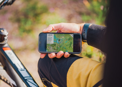 En person håller i en mobiltelefon med en öppen karta över leder, sittandes vid en cykel.
