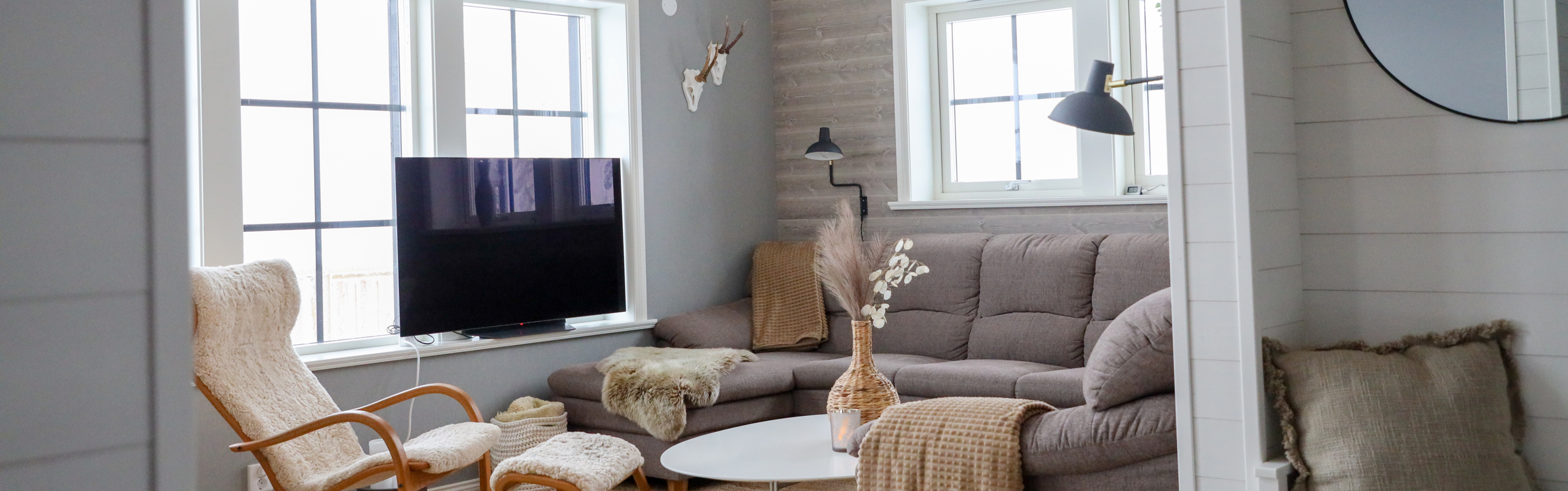 Bright living room with corner sofa, armchair, TV and large windows.