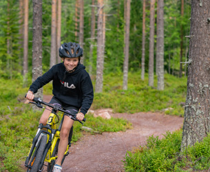 Flicka med hjälm cyklar på en stig i skogen på en gul mountainbike.