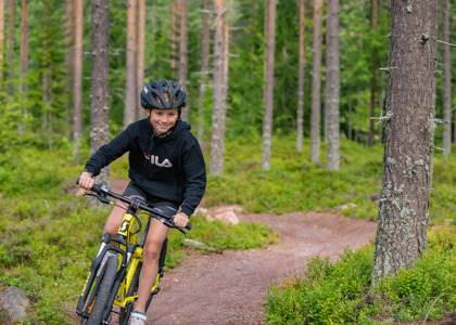 Pige med hjelm cykler på en skovsti på en gul mountainbike.