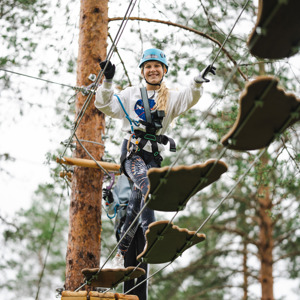 Tjej som går över hinder där man hoppar över plankor i form av fötter i grönklitts Klätterpark